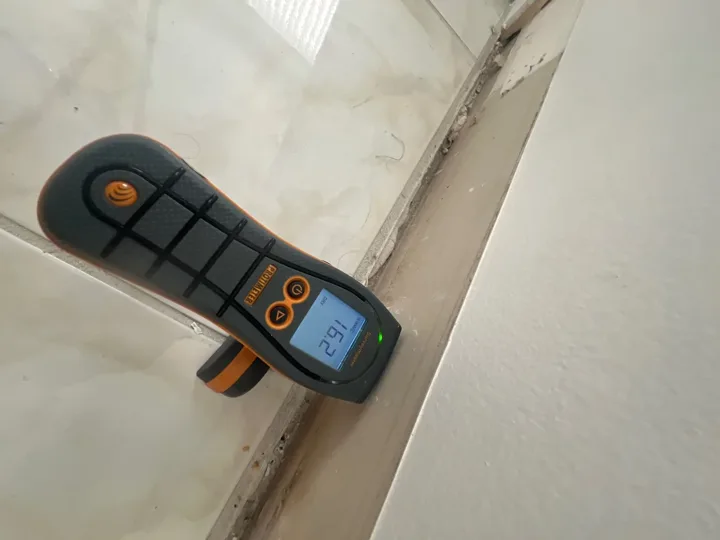 Moisture meter positioned against an interior wall near the baseboard.